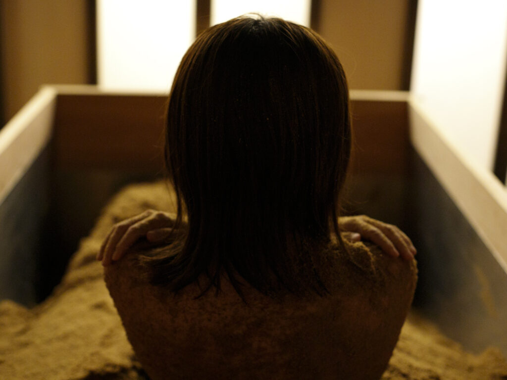 障子のあかりを背に、浴槽（桶）の中で静かに過ごす女性の後ろ姿