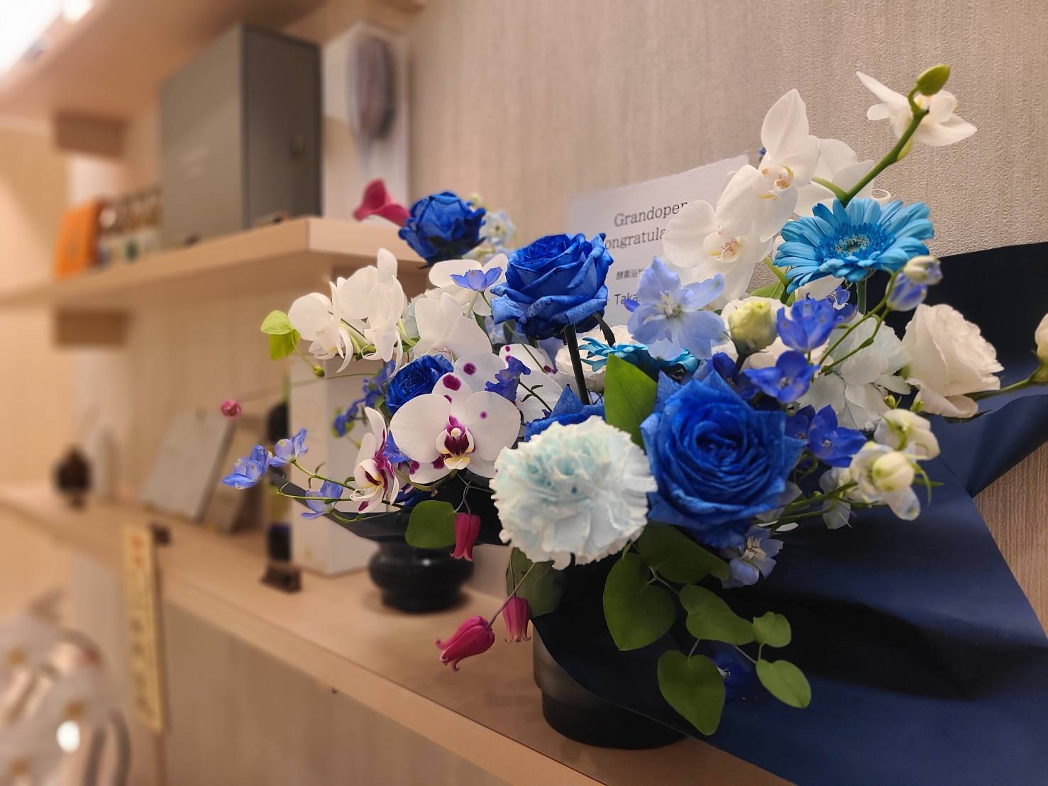 青いバラやガーベラ、白い胡蝶蘭をあしらった、開店祝いのアレンジメント。