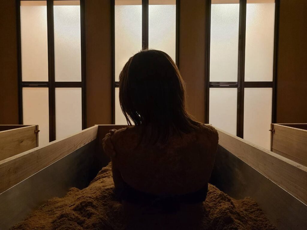 障子のあかりを背に、酵素浴の桶に身を起こす女性のシルエット