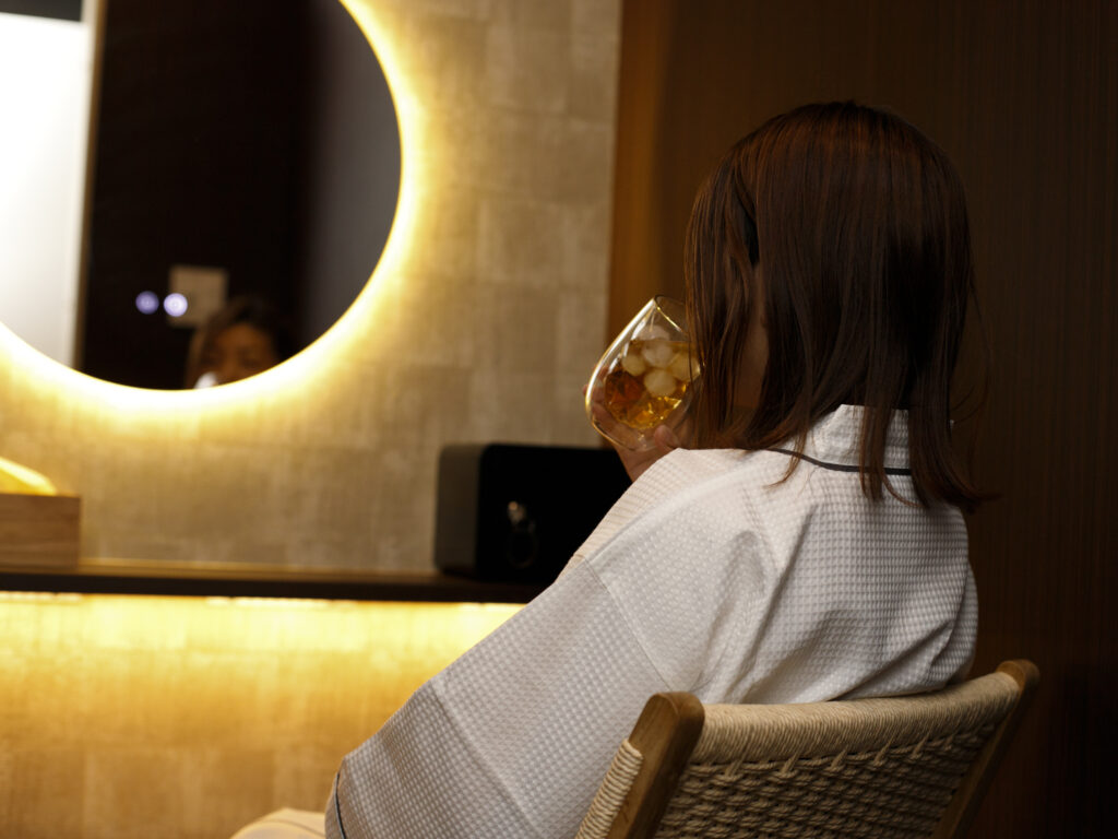 半個室の休憩ルームで、鏡の前の椅子に腰かけてひと息つく女性の後ろ姿。